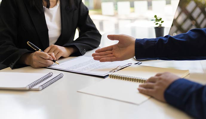Close up of two business professionals in suits discussing and signing a legal contract or service agreement at a desk