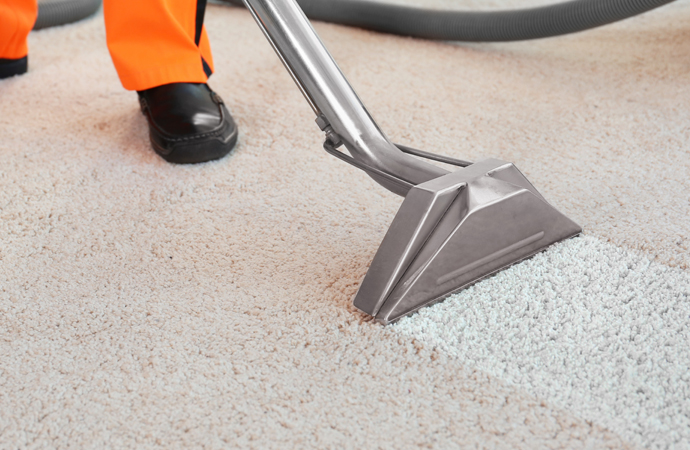 An employee at a dry cleaners meticulously removes dirt from a carpet in a flat.