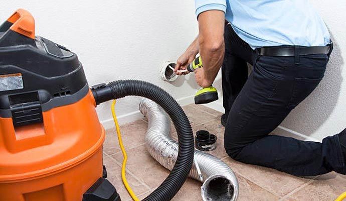 Technician cleaning a dryer vent duct with a vacuum and drill