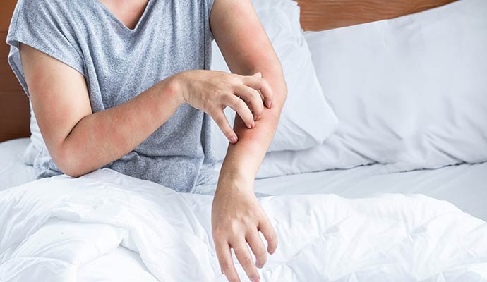 Person sitting in bed scratching an itchy arm