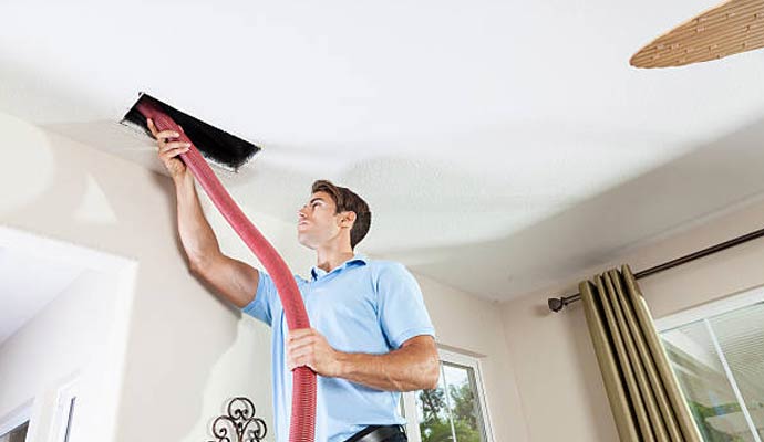 A professional technician using a high-powered vacuum hose to clean a residential ceiling air duct