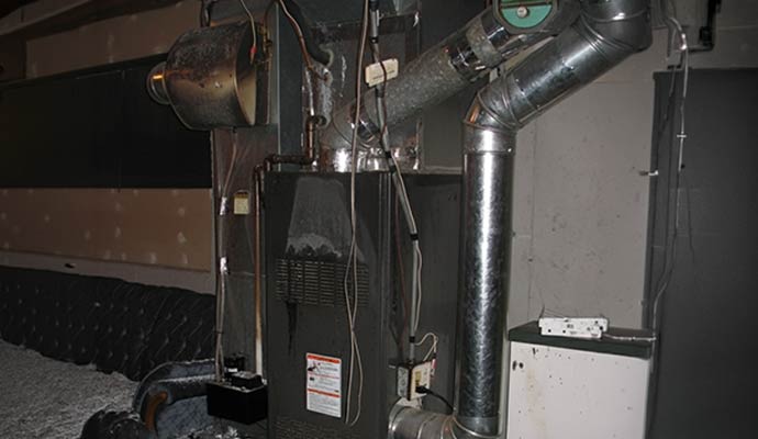 Close up of a residential furnace and HVAC ventilation system covered in black soot and smoke residue after a fire