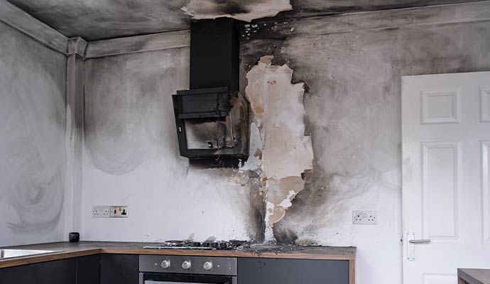 Smoke damaged kitchen wall with soot stains and peeling paint above the stove
