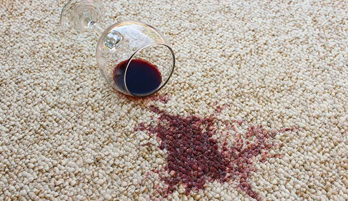 An overturned wine glass with a large red wine stain on a light-colored residential carpet