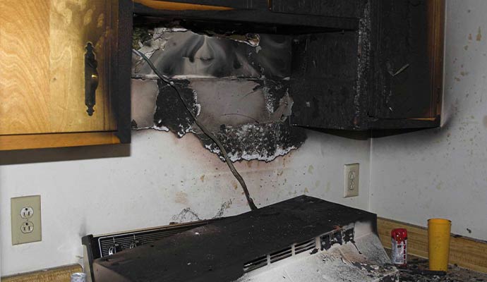 Severe fire and soot damage on a kitchen stove vent hood and wooden cabinets