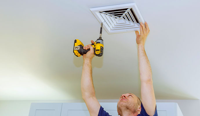 Technician servicing a ceiling ventilation vent