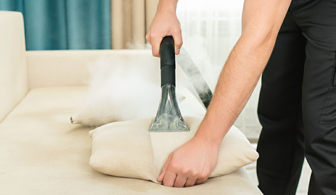 Technician steam cleaning a throw pillow with a professional extraction tool