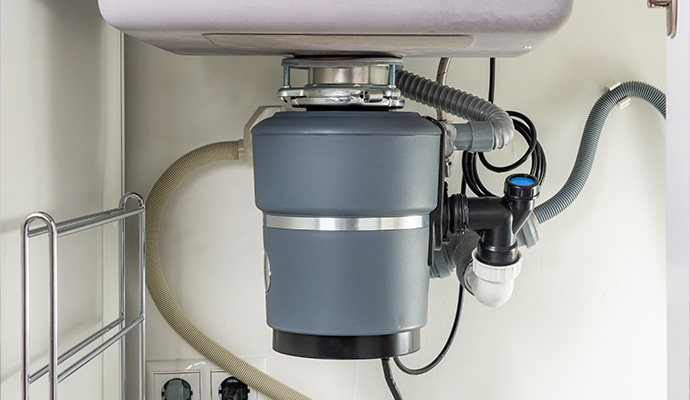 Garbage disposal unit under a kitchen sink connected to plumbing pipes